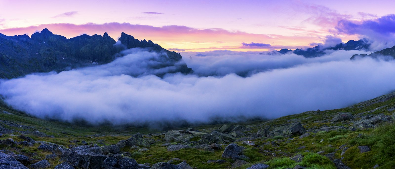 Un mare di nuvole tra le montagne all'alba, con il cielo viola e rosa